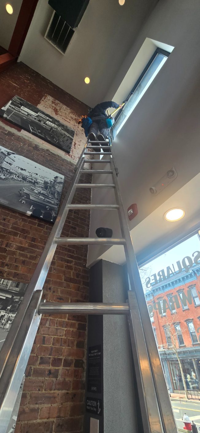 Cleaning tall interior restaurant windows from an extension ladder